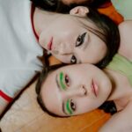 Dvě ležící dívky s namalovanými gelovými linkami na očích.