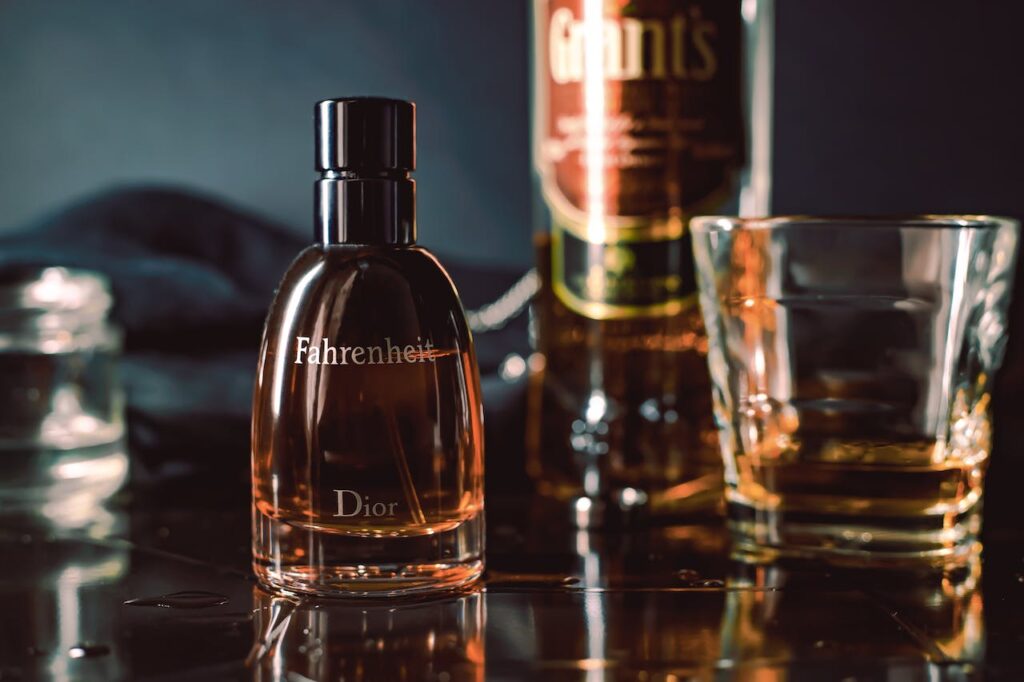 Parfém Fahrenheit od Diora na pozadí láhve whiskey se sklenicí.