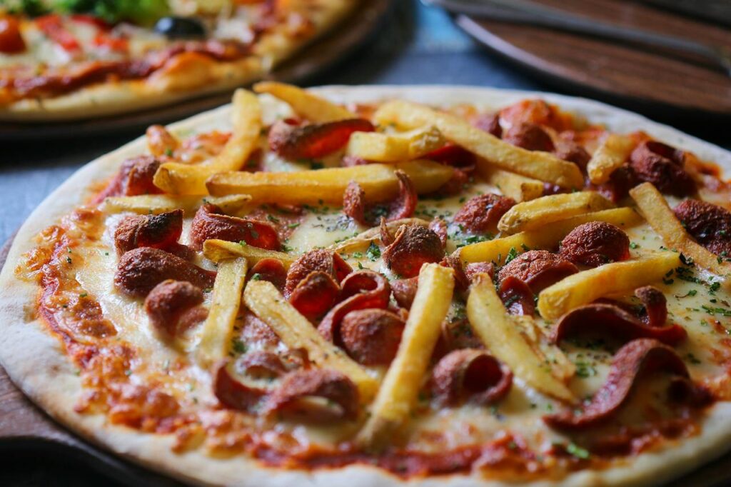 Pizza zdobená uzeninou a hranolky.