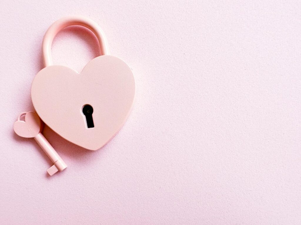 Růžový klíč s růžovým zámkem ve tvaru srdce na růžovém pozadí.