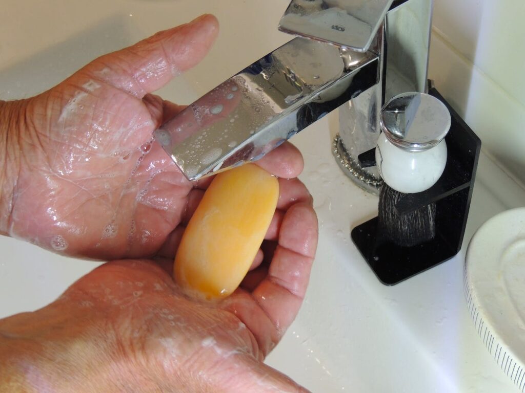 Mokré namydlené ruce držící mýdlo.
