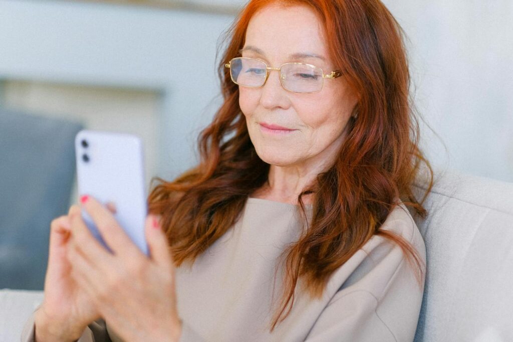 Starší žena s dlouhými vlasy hledící do mobilu.