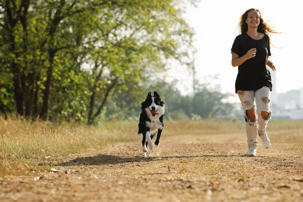 Smějící se žena, běžící v přírodě po boku svého psa.