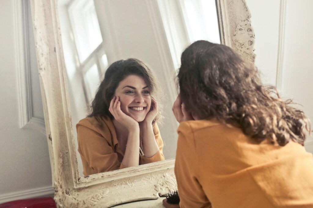 Smějící se žena hledící na sebe do zrcadla.