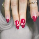 Červené nehty zdobené nápisem Love.