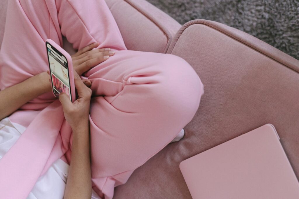 Detail na dívku sedící na gauči v růžových teplácích s mobilem v rukou.