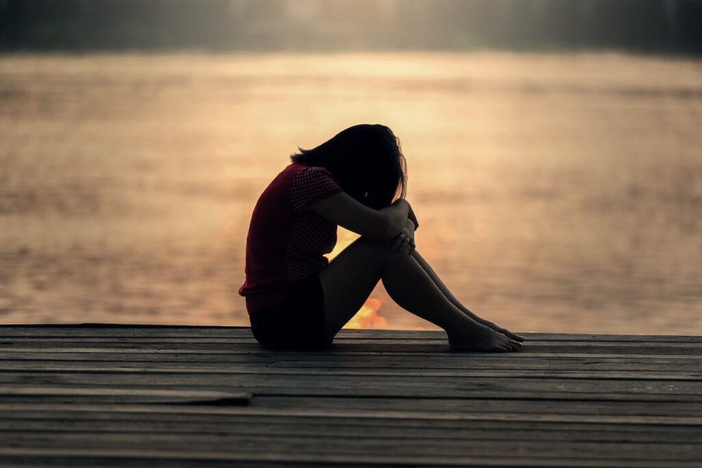 Smutná dívka sedící na mole při západu slunce.