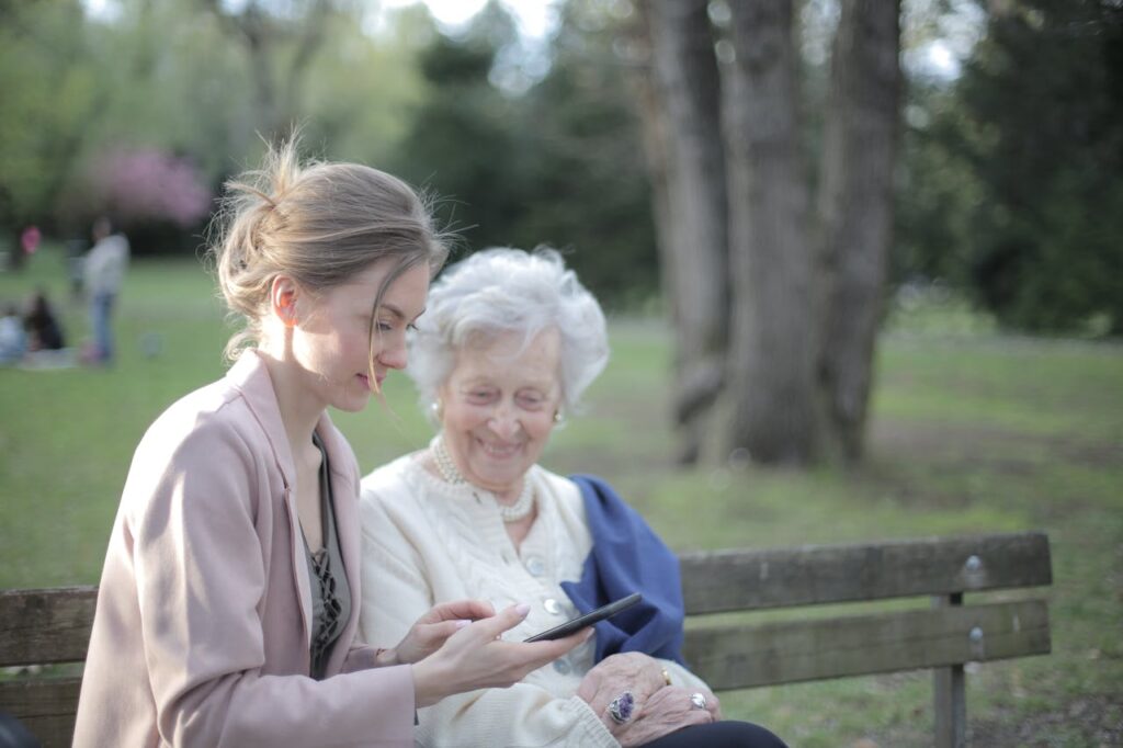 Starší a mladší usmívající se ženy sedící na lavičce v parku.