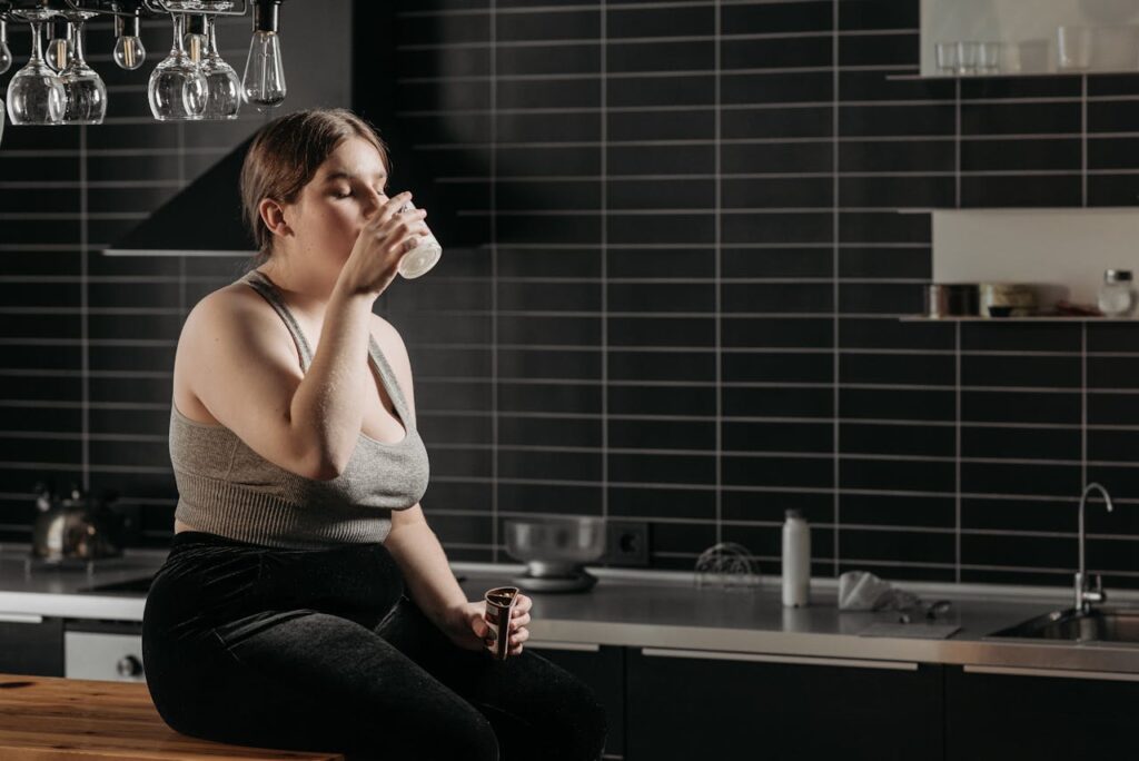 Obézní dívka pijící vodu v kuchyni.