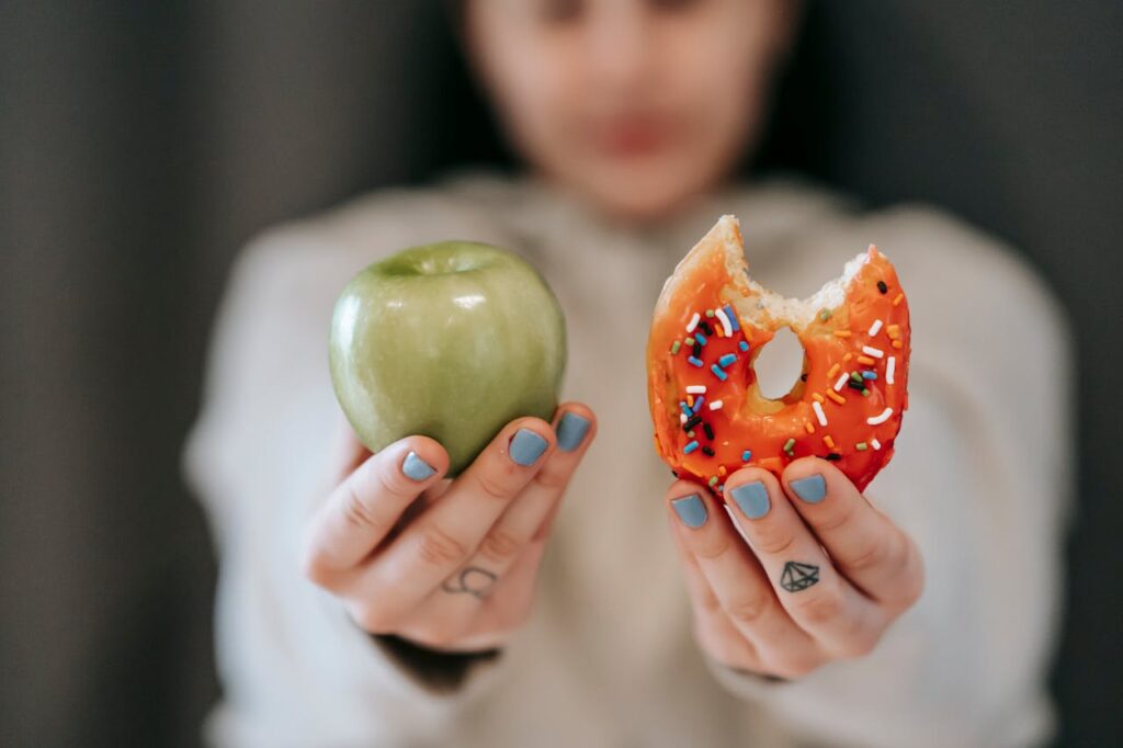 Detail na ruce držící jablko a koblihu.