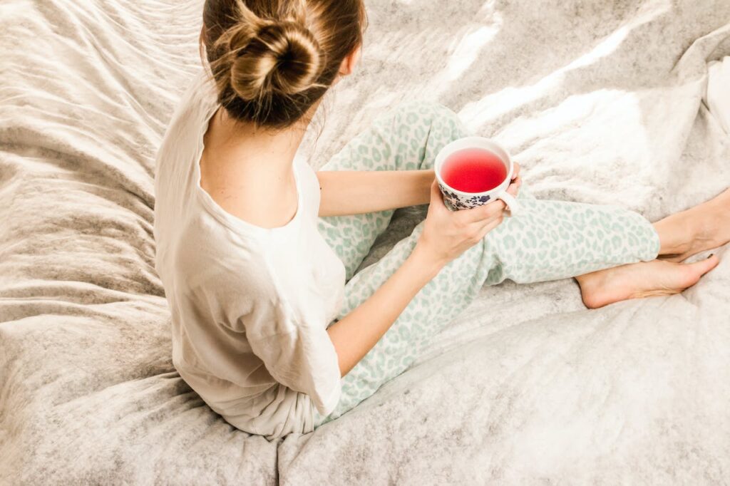 Žena sedící s šálkem čaje v posteli. 