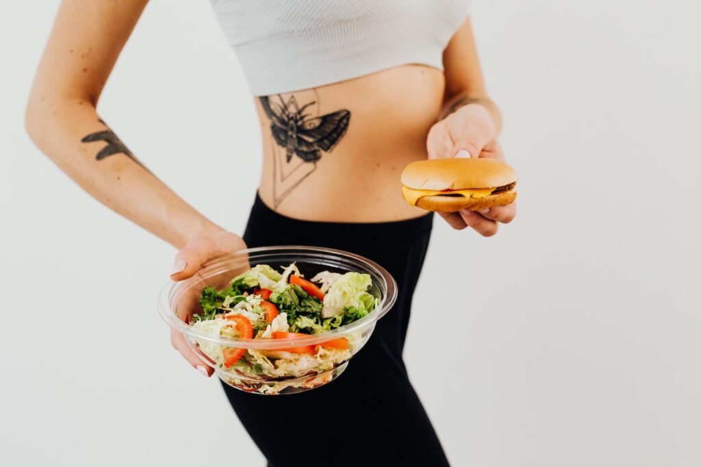 Štíhlá dívka držící salát a hamburger.