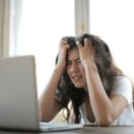 Nešťastná žena držící se za hlavu sedící u počítače.
