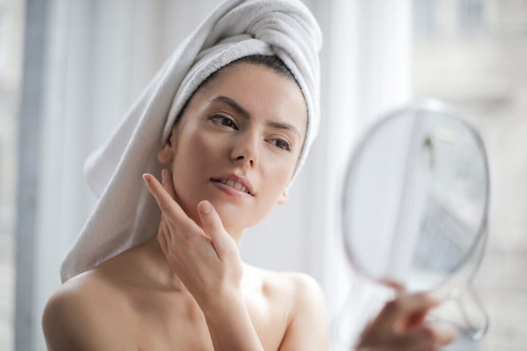 Žena s umytými vlasy v turbanu hledící do zrcadla.