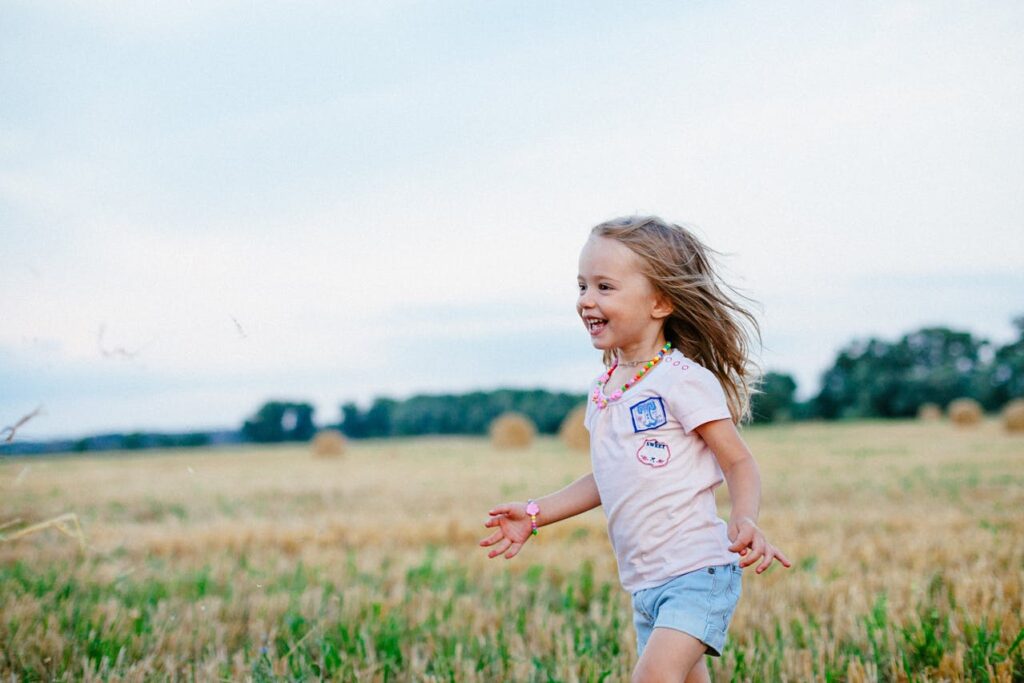 Šťastná usměvavá holčička běžící po poli.