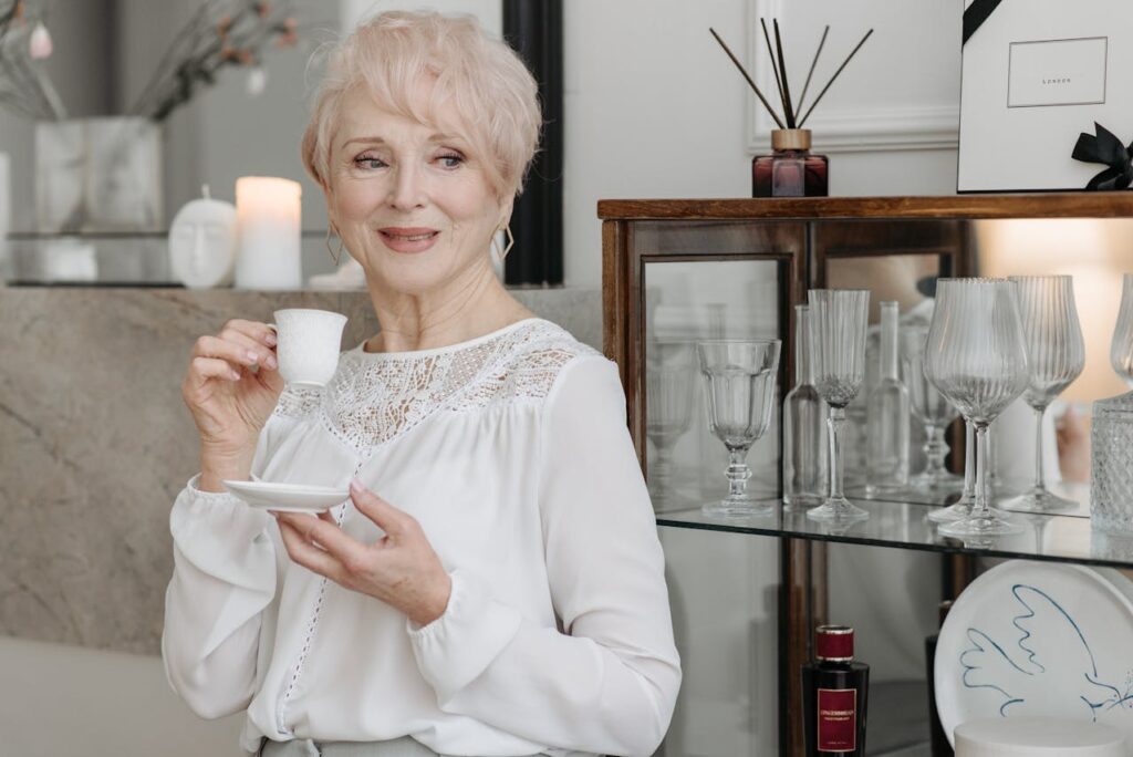 Starší elegantní dáma v bílé blůze pijící kávu.