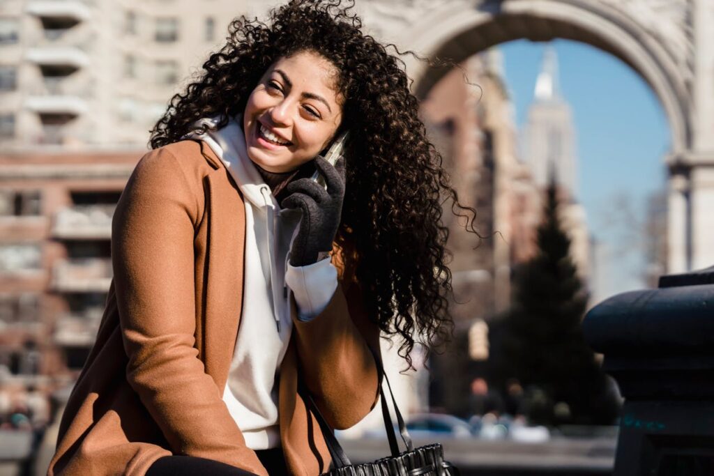 Smějící se žena s mobilem u ucha v jarním kabátu.