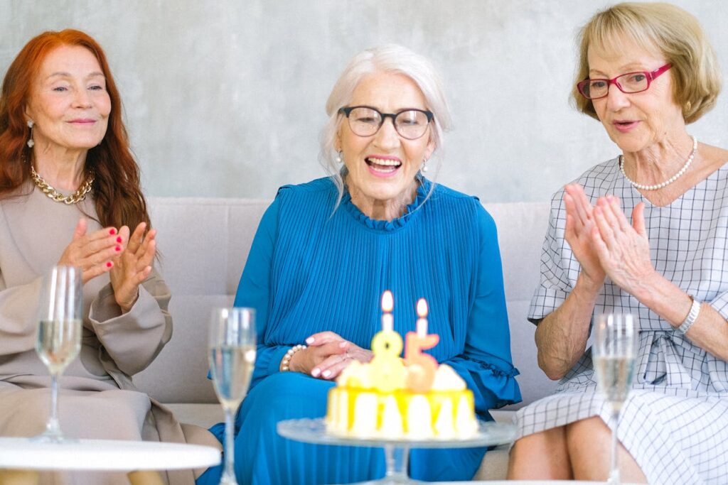 Starší oslavující dámy s dortem a sklenicemi šampaňského.