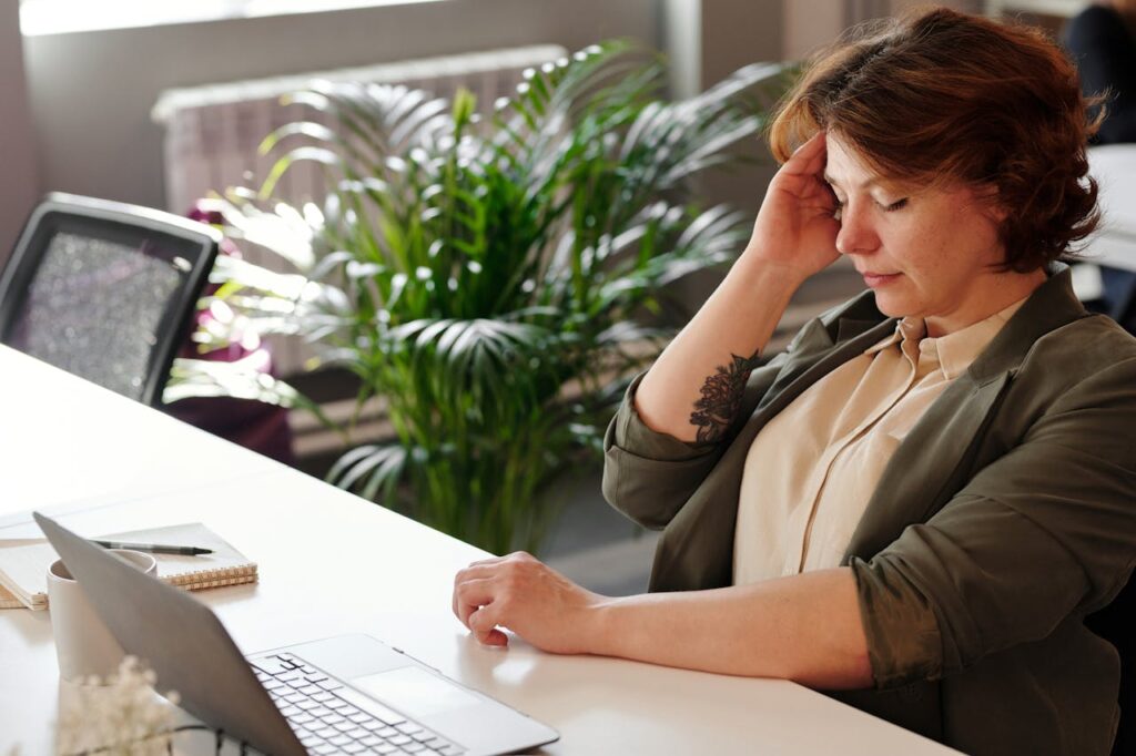Žena s bolestí hlavy sedící u počítače.