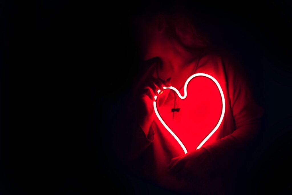 Žena držící svítící srdce ve tmě.