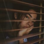 a woman looking out of a window with blinds